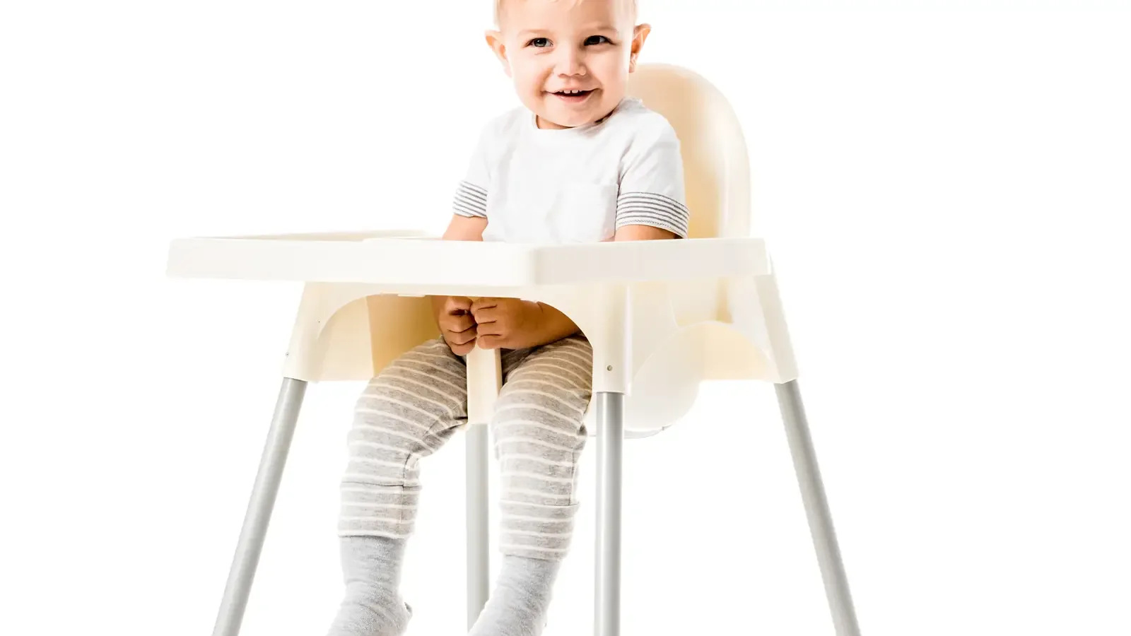 A toddler boy in a blue party hat smiling, sitting in a highchair, against a white background