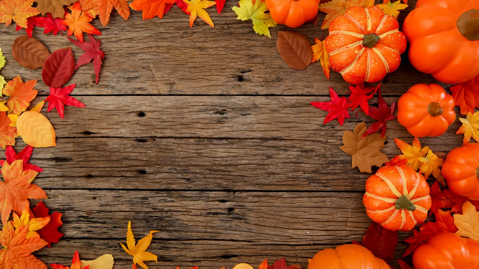 Fall leaves and small pumpkins framing a rustic dark wooden table