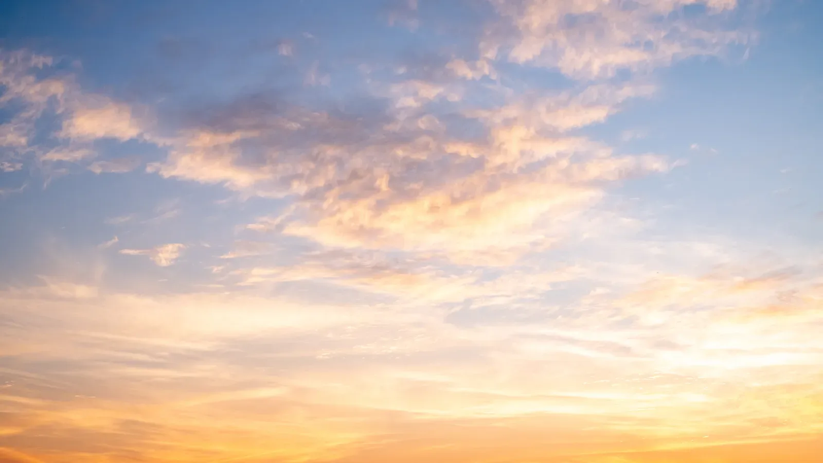 Golden sunrise light spreading through soft clouds across an open sky