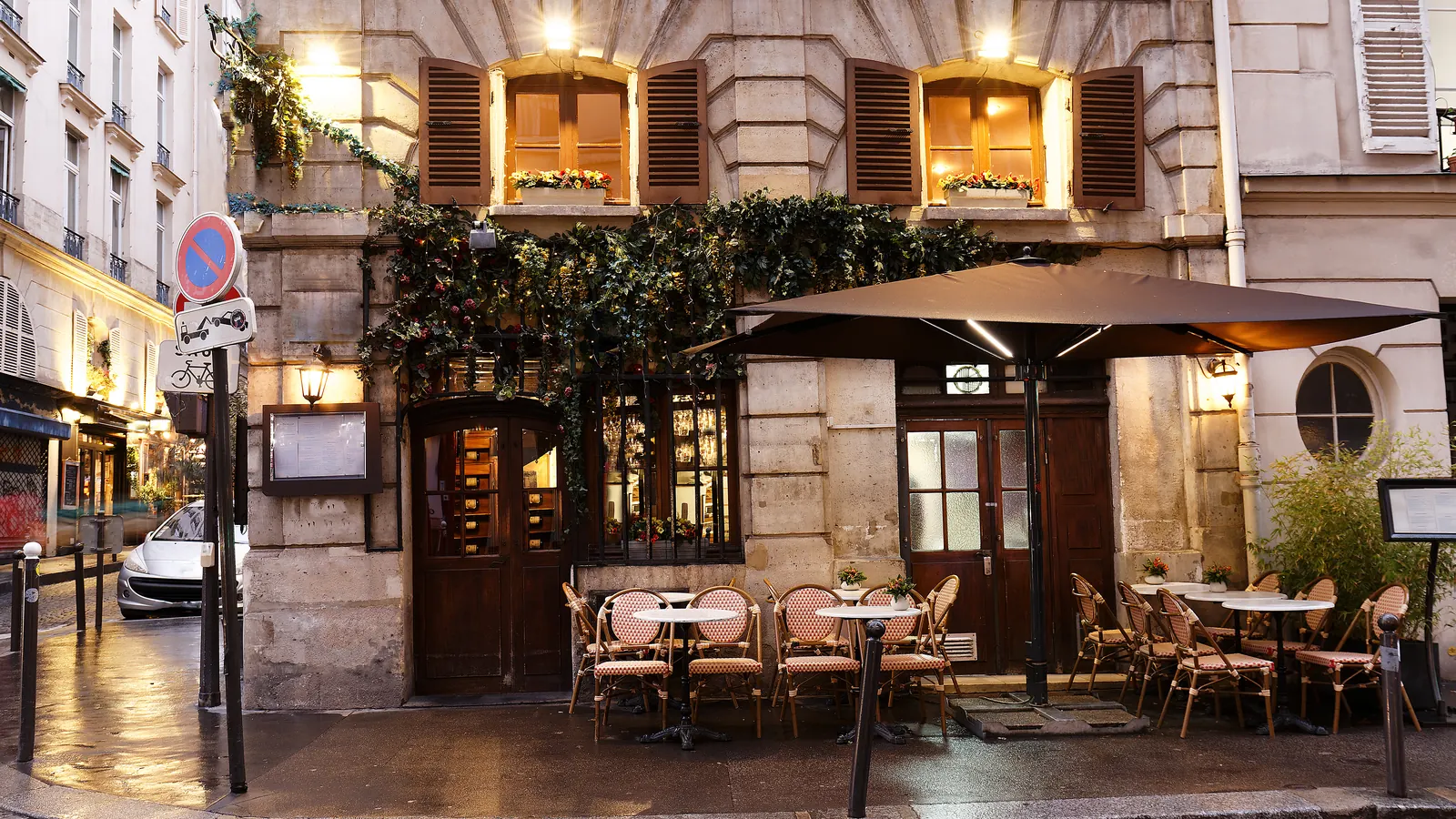 A traditional Paris street cafe at dusk, with awnings, warm lights and tables out on the sidewalk