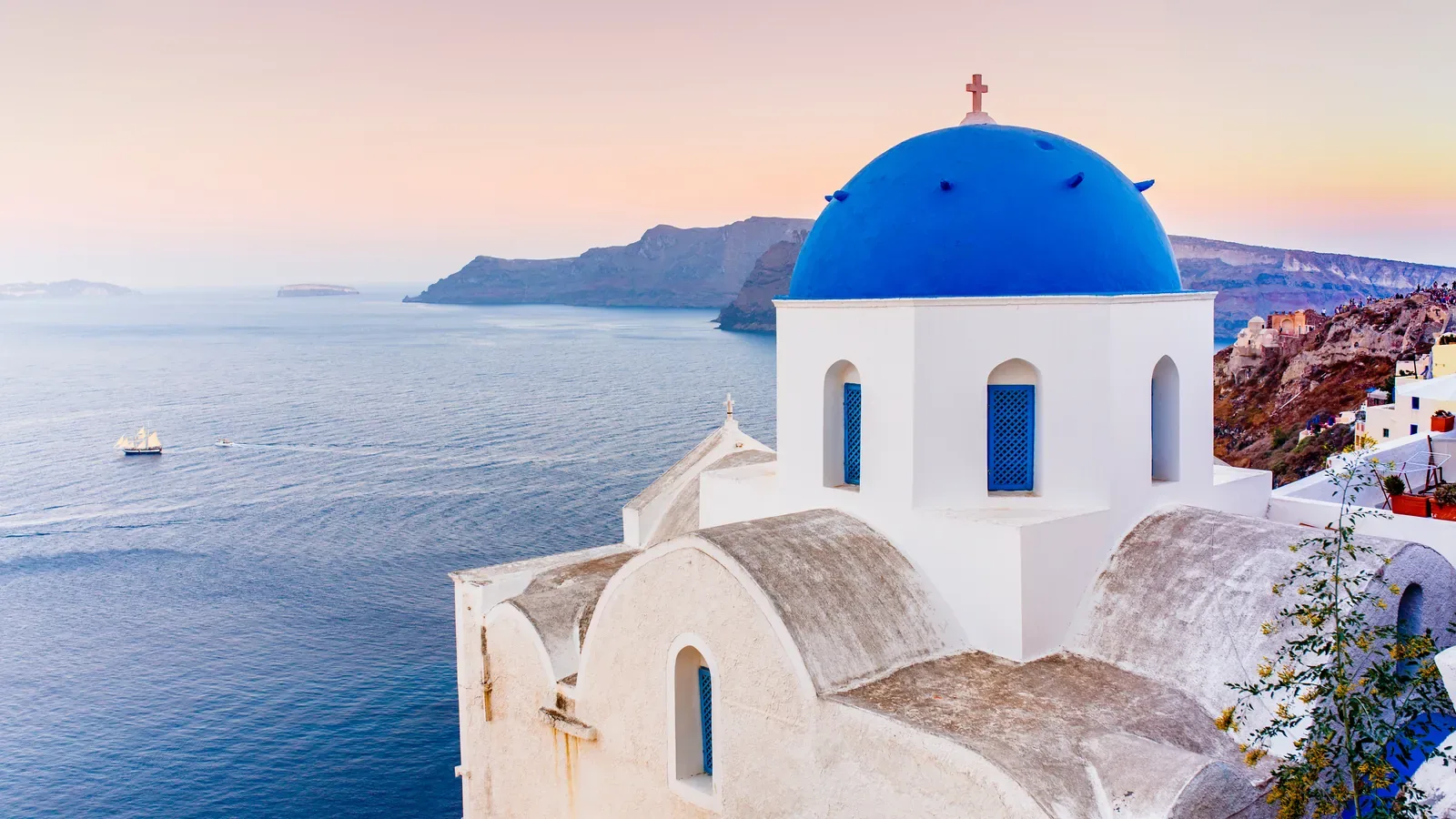 A white Greek Orthodox church with a blue dome overlooking the sea at sunset on Santorini