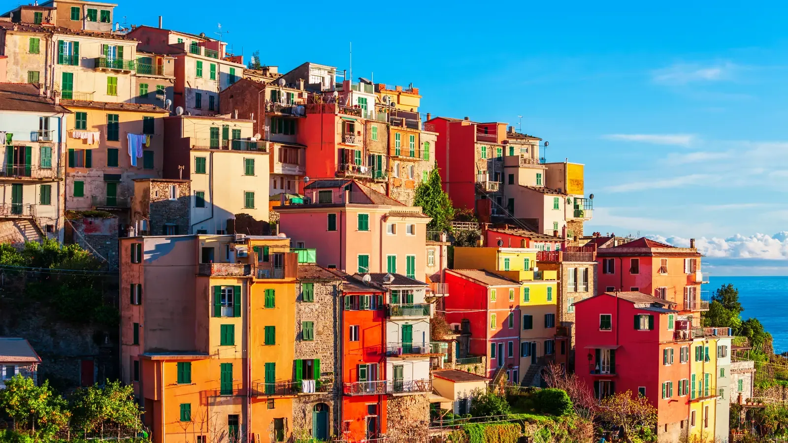 Brightly painted houses in orange, red and yellow stacked up a steep hillside above the sea in an Italian coastal village
