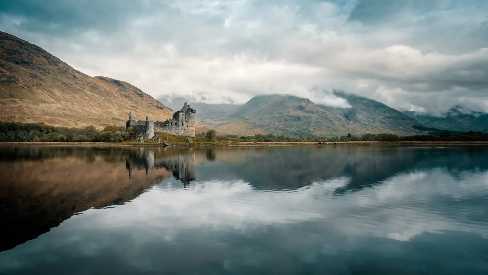 Kilchurn Castle reflected in the still water of Loch Awe under a gray Highland sky