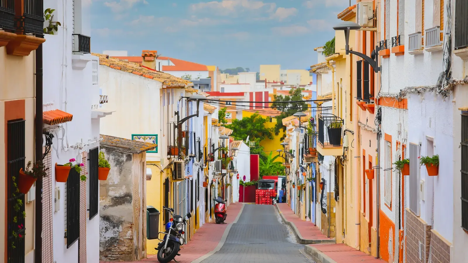A narrow Spanish street lined with pastel-painted houses and flower pots under a bright blue sky