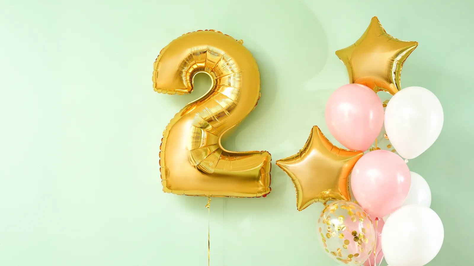 Gold number two foil balloon with pink and gold balloons on a mint green background