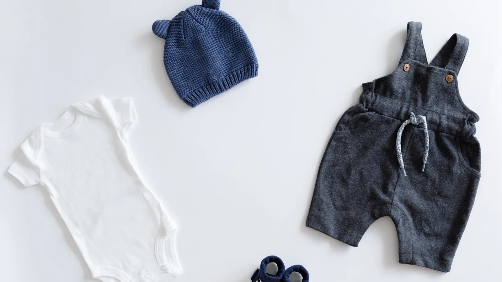 Flat lay of neutral baby boy clothes laid out for a new sibling