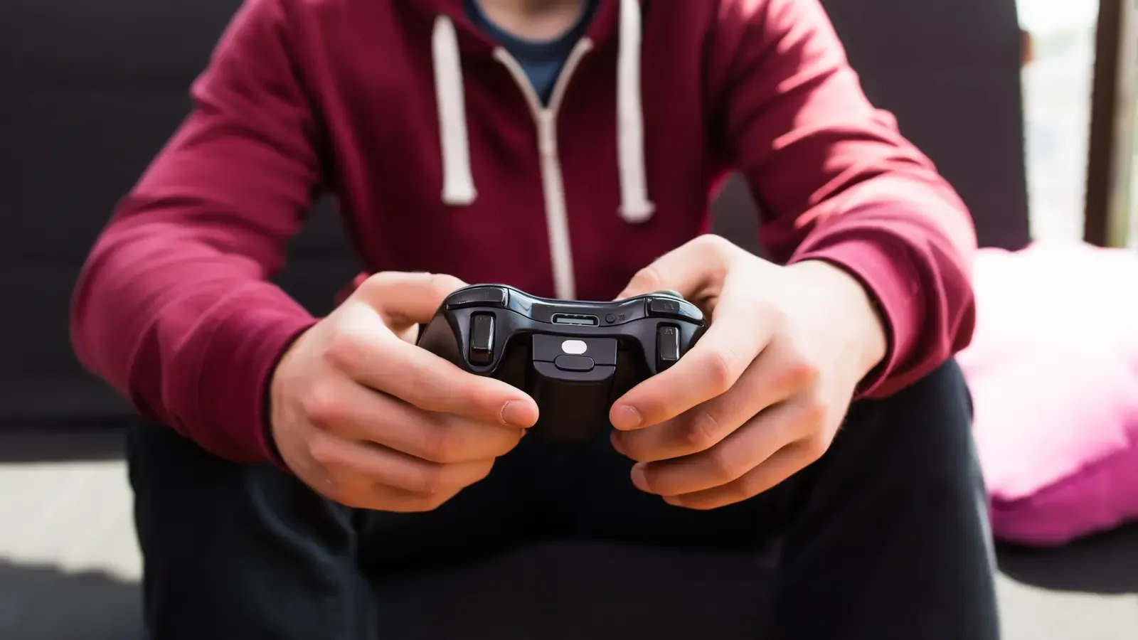 A boy in a red hoodie holding a video game controller in both hands