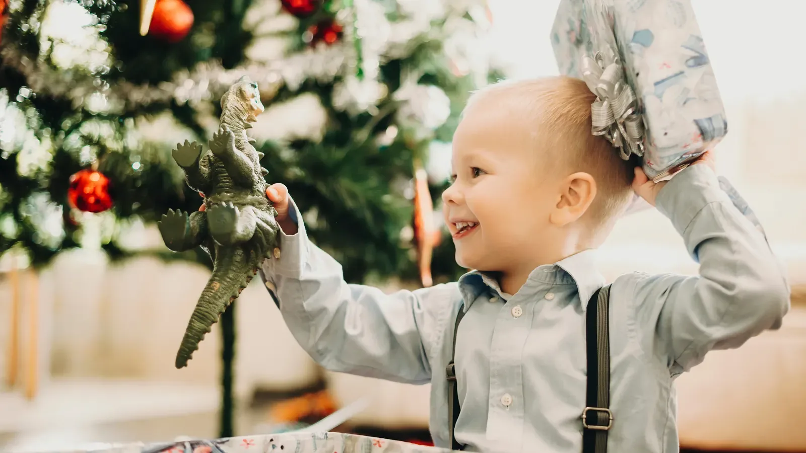 An excited toddler boy receiving a wrapped dinosaur toy for Christmas