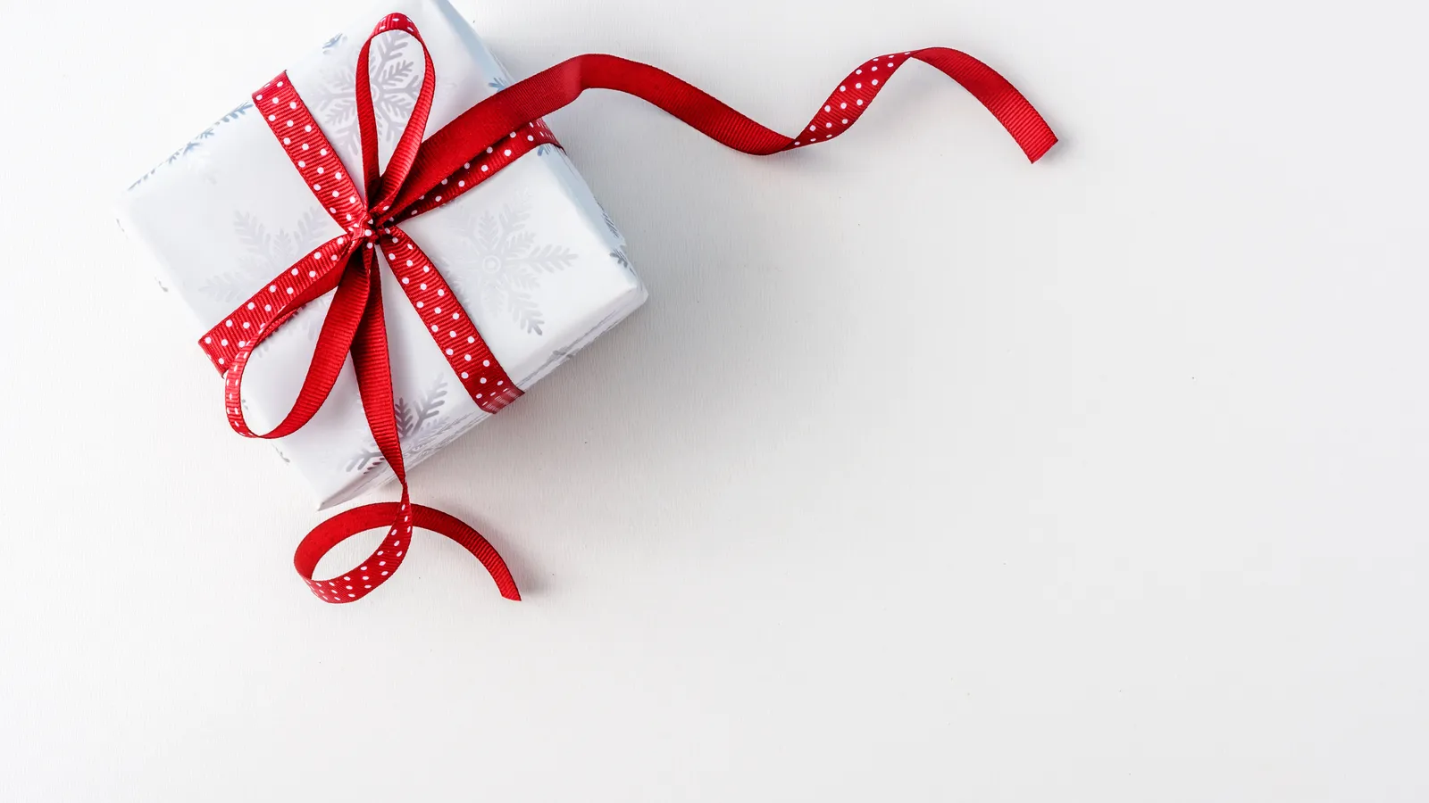 A single Christmas present wrapped in white paper with a red ribbon on a white background