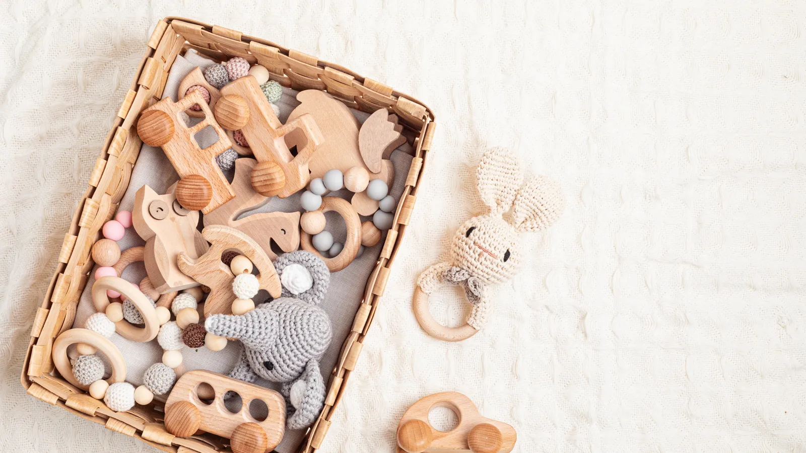 Basket of wooden baby toys, rattles and a wooden car on a cream blanket
