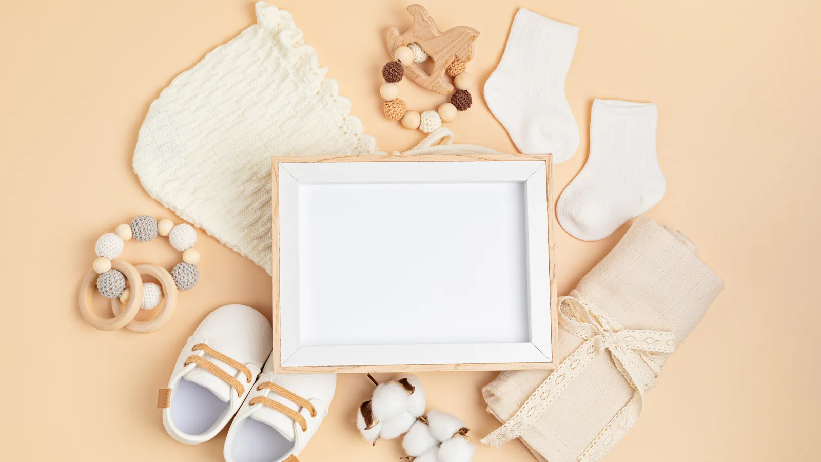 Empty wooden photo frame surrounded by baby shoes, socks and knitted items on a warm neutral background