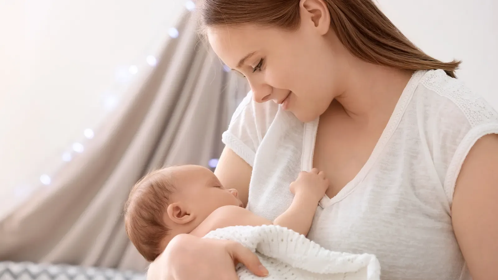A mother smiling down at the newborn baby she is holding wrapped in a white blanket