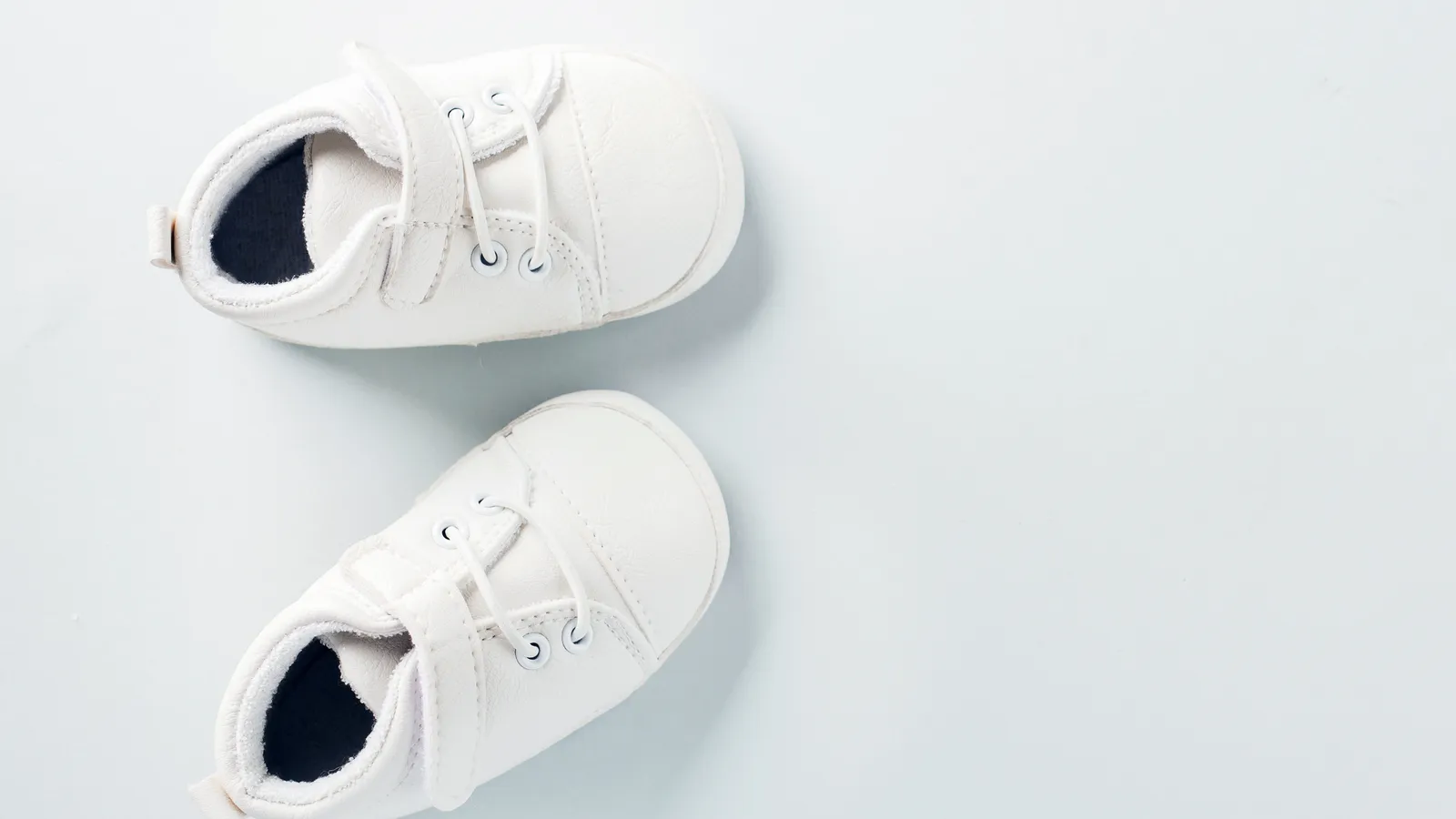 A pair of small white baby shoes on a pale blue-gray background
