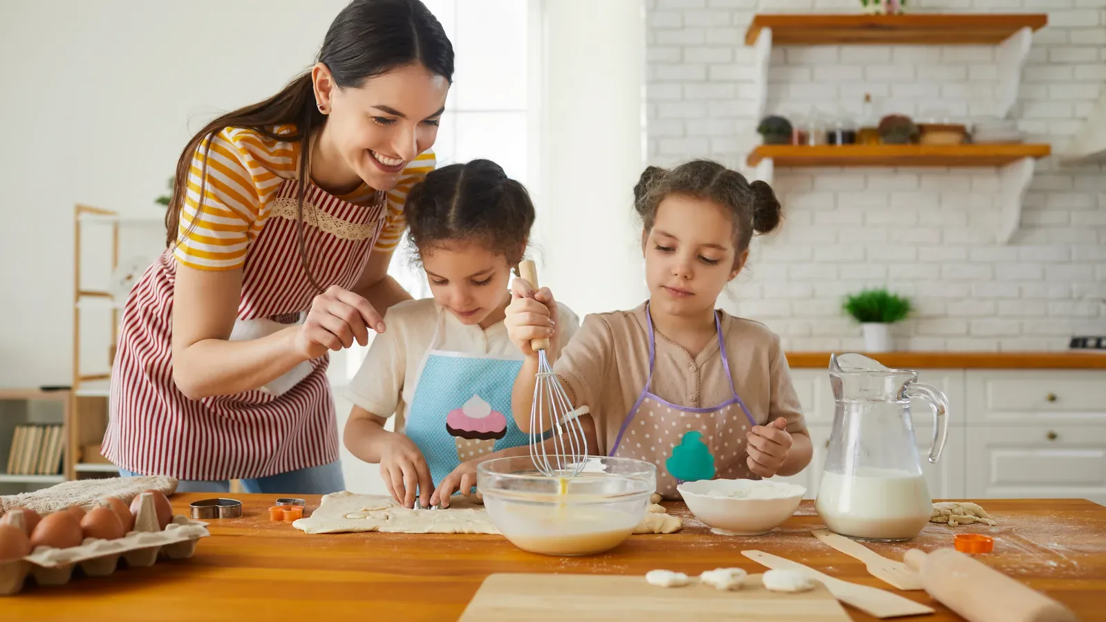 An adult and two children baking together at a kitchen counter, mixing batter in a bowl with a whisk