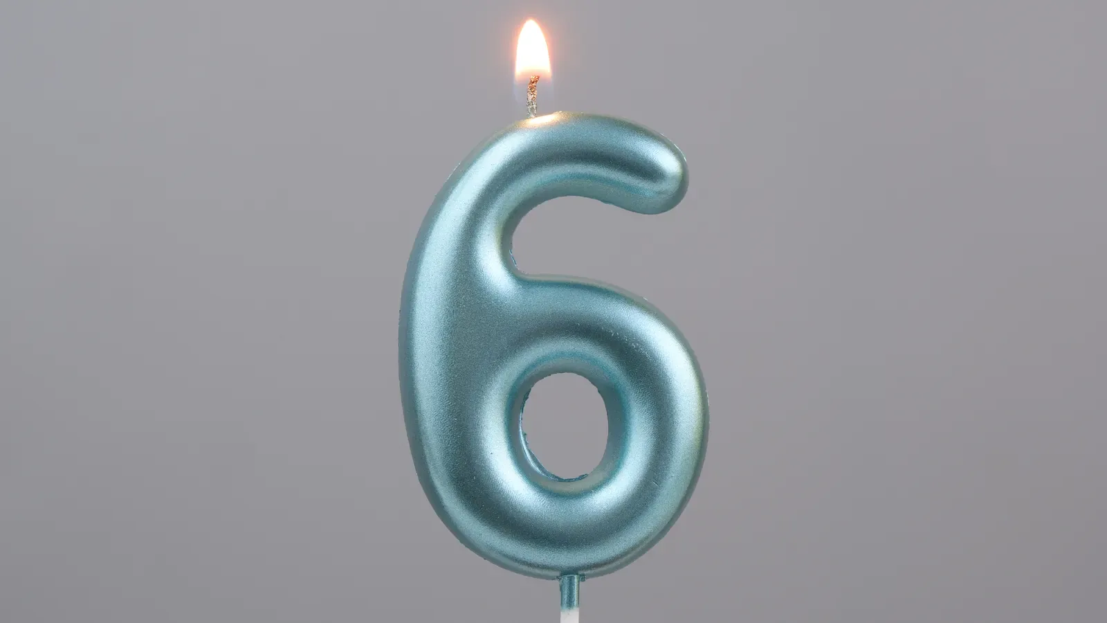 A blue number six birthday candle burning on a cake against a gray background