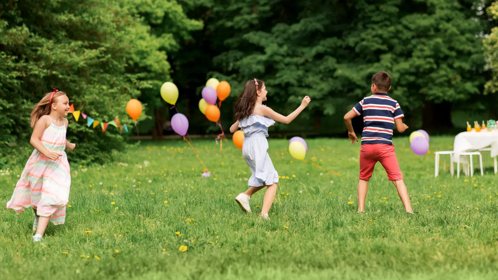 Children running and playing tag with balloons on a sunny lawn at a birthday party