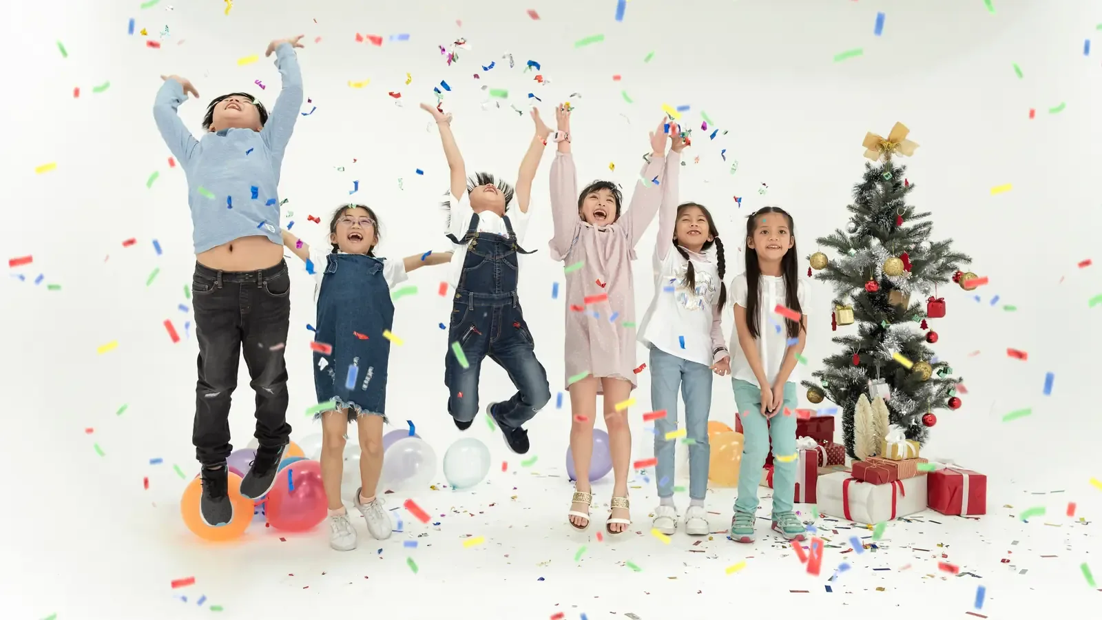 A group of children jumping and cheering in a shower of confetti next to a Christmas tree