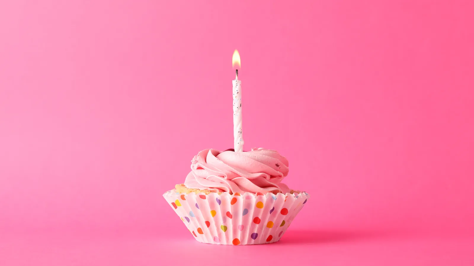 A single cupcake with a lit candle on a pink background